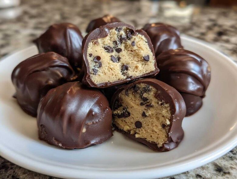 Close-up of several chocolate-dipped No-Bake Chocolate Chip Cookie Dough Truffles, one cut in half showing the dough inside.