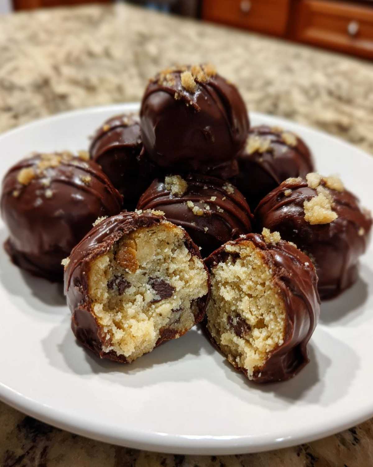 A plate of No-Bake Chocolate Chip Cookie Dough Truffles dipped in chocolate and topped with nuts.