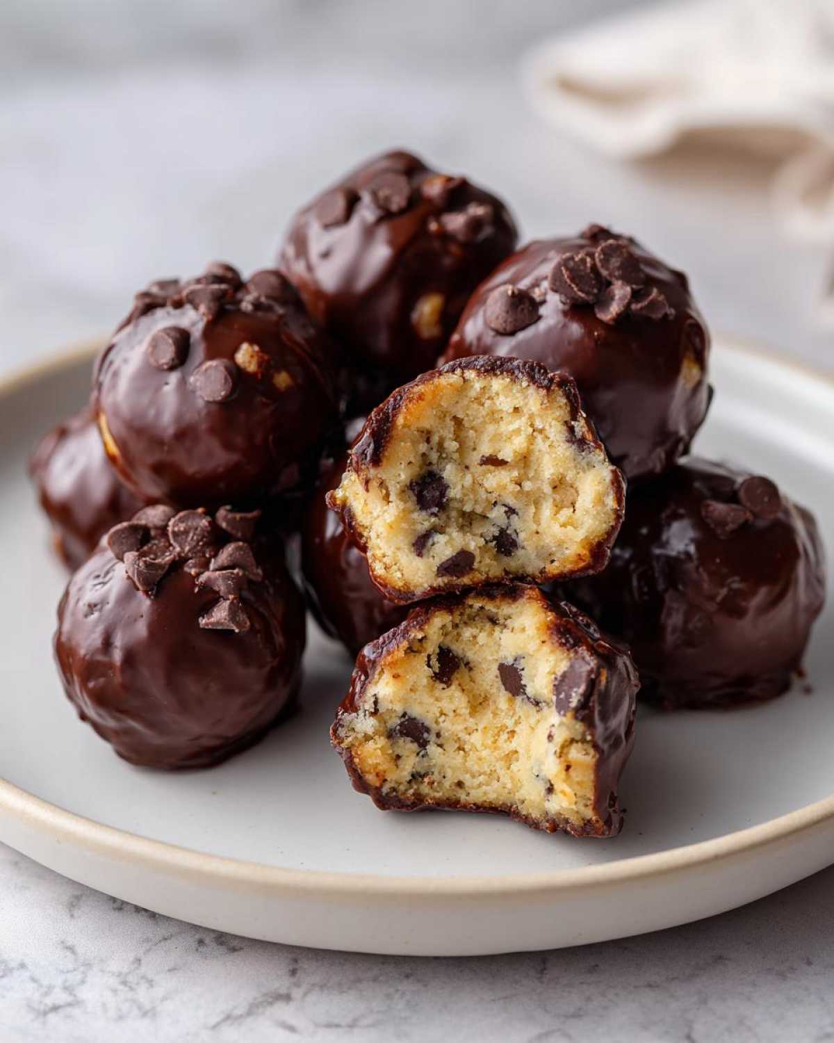 A stack of No-Bake Chocolate Chip Cookie Dough Truffles dipped in dark chocolate and topped with mini chips.