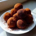 A mound of rich, dark No-Bake Chocolate Orange Truffles heavily dusted in cocoa powder on a white plate.