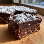 A square portion of No-Bake Coconut Chocolate Date Bars showing a dense base and thick chocolate topping sprinkled with shredded coconut.