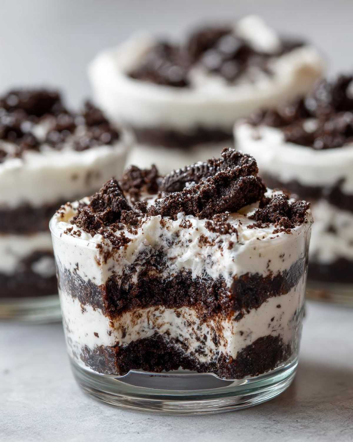 A close-up of a layered No-Bake Cookies and Cream Pie Cup with a bite taken out, showing cream and crushed cookies.