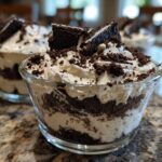 Two glass cups filled with layered No-Bake Cookies and Cream Pie Cups, topped with whipped cream and cookie crumbles.
