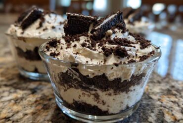 Two glass cups filled with layered No-Bake Cookies and Cream Pie Cups, topped with whipped cream and cookie crumbles.