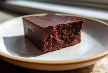 A single, thick square of rich, dark No-Bake Espresso Chocolate Fudge on a light ceramic plate.