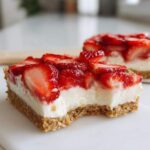 Close-up of a square of No-Bake Strawberry Cheesecake Bark with a bite taken out, showing graham cracker crust and creamy filling.