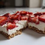 Close-up of two squares of No-Bake Strawberry Cheesecake Bark showing thick creamy filling and fresh strawberry topping on a graham cracker crust.