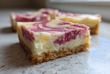 A close-up of a square No-Bake Strawberry Lemon Cheesecake Bars showing a graham cracker crust and a swirled berry topping.
