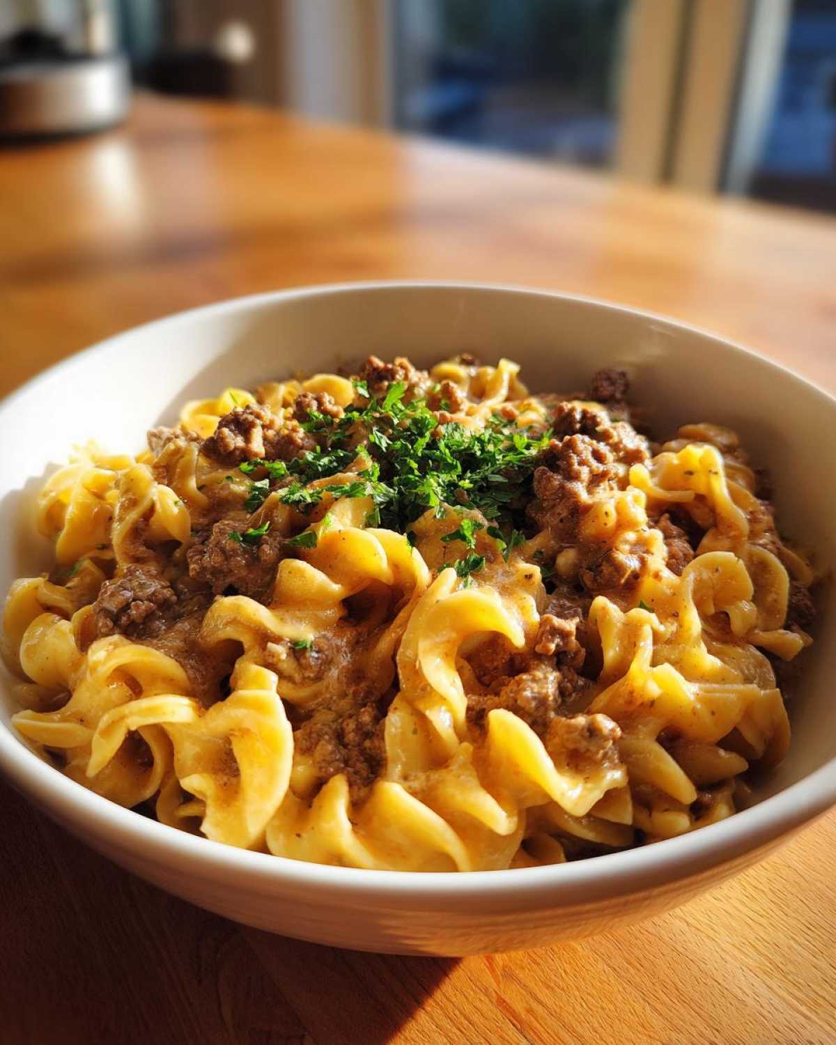 A close-up of a white bowl filled with One-Pot Creamy Garlic Butter Beef and Noodles, topped with parsley.