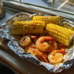 Close-up of cooked shrimp and corn on the cob seasoned with Cajun spices in a foil packet.