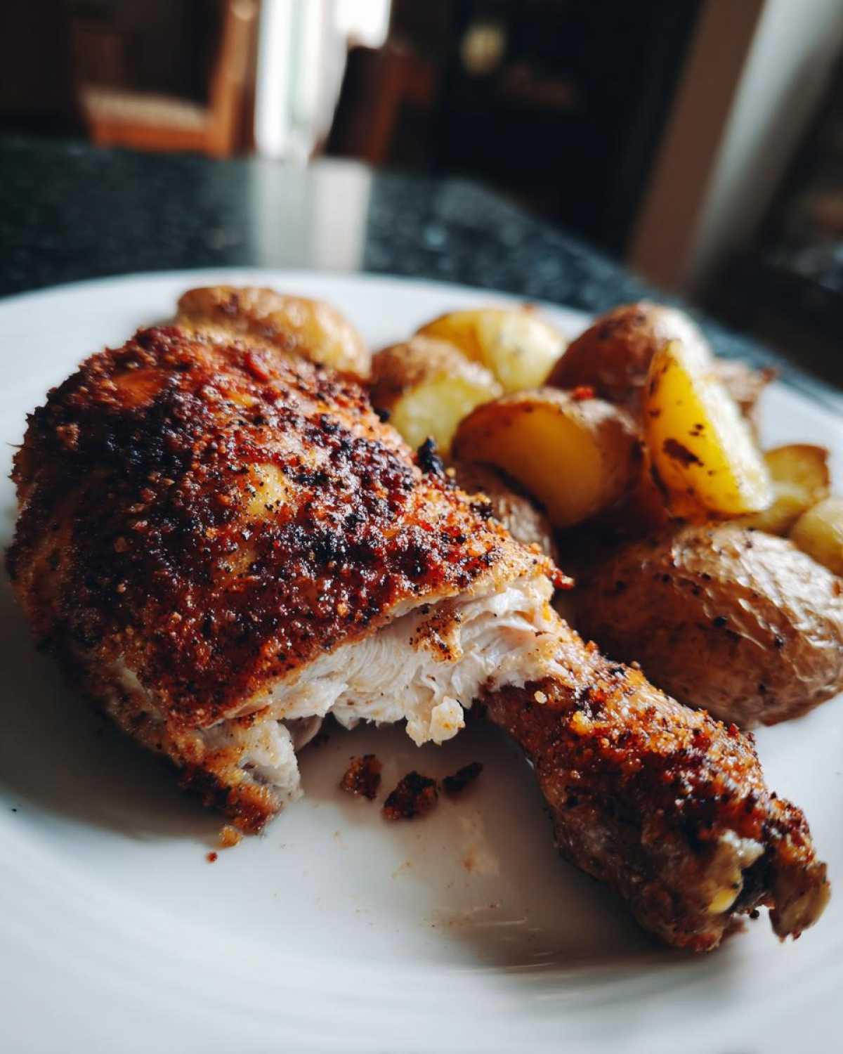 Close-up of a juicy Sheet Pan Garlic Parmesan Chicken Drumstick broken open next to roasted potatoes.