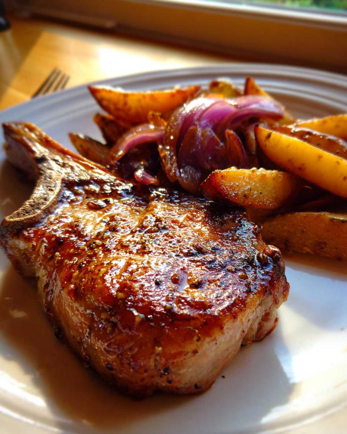 Close-up of a glazed Sheet Pan Maple Dijon Pork Chop served with roasted potatoes and red onion wedges.