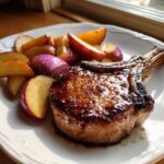 A perfectly cooked, glazed pork chop served with roasted apple slices and red onion wedges, showcasing Sheet Pan Maple Dijon Pork Chops.