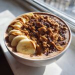 Close-up of a rich Vegan Chocolate Peanut Butter Banana Smoothie Bowl topped with banana slices, granola, and peanut butter drizzle.