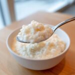 A spoonful of thick, creamy Vegan Creamy Coconut Rice Pudding being lifted from a white bowl.