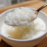 A spoonful of thick, creamy Vegan Creamy Coconut Rice Pudding being lifted from a white bowl.