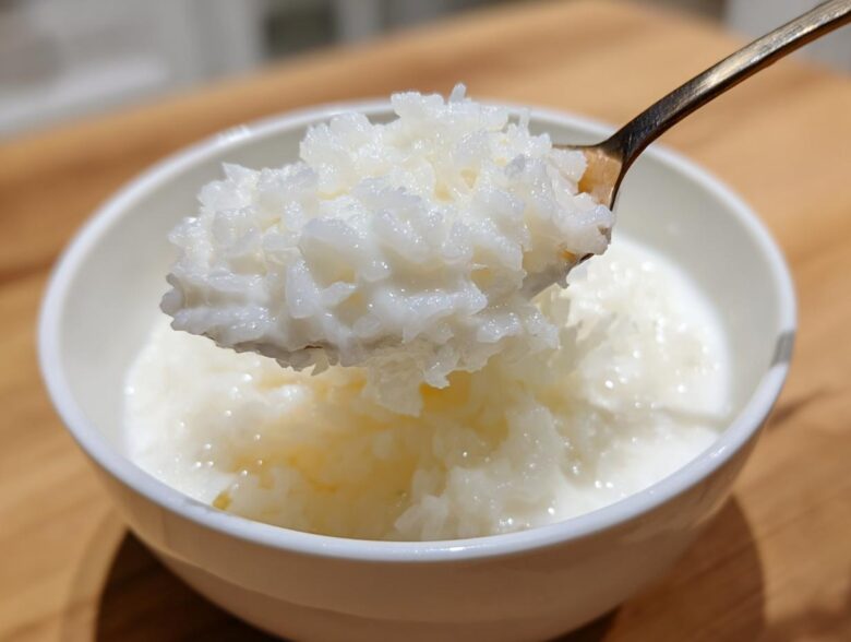 A spoonful of thick, creamy Vegan Creamy Coconut Rice Pudding being lifted from a white bowl.
