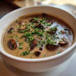A close-up of rich Vegan Creamy Mushroom Soup with Thyme, topped with sautéed mushrooms and fresh parsley.