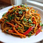 A close-up of Vegan Creamy Peanut Noodle Salad tossed with julienned carrots, red peppers, and fresh cilantro.