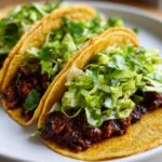 Close-up of three Vegan Easy Black Bean Tacos filled with dark seasoned filling and topped with bright green cilantro lime slaw.
