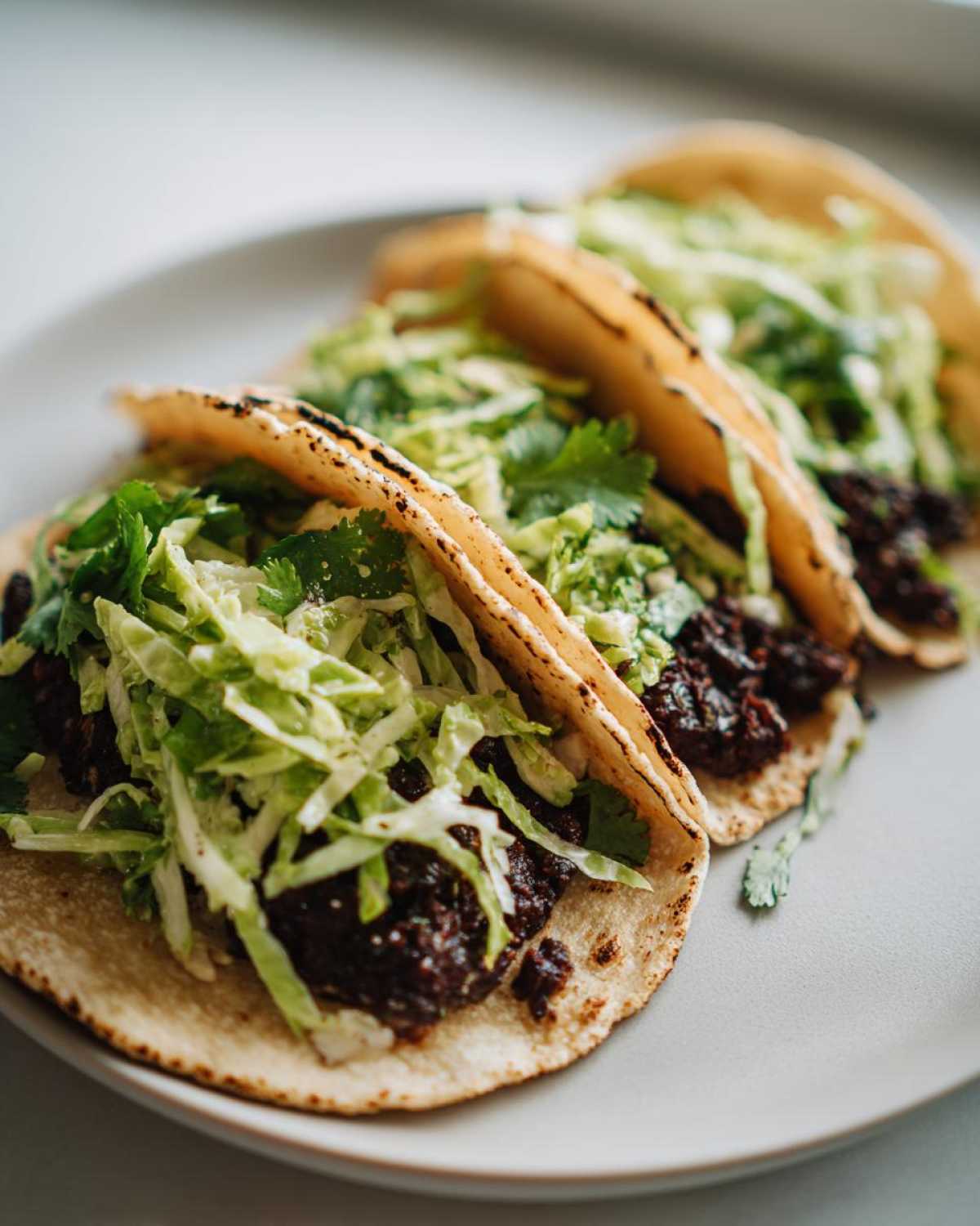 Three Vegan Easy Black Bean Tacos filled with black bean mash and topped with bright green cilantro lime slaw.
