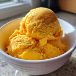 Three bright orange scoops of Vegan Mango Pineapple Sorbet served in a white dessert bowl.