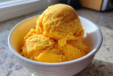 Three bright orange scoops of Vegan Mango Pineapple Sorbet served in a white dessert bowl.