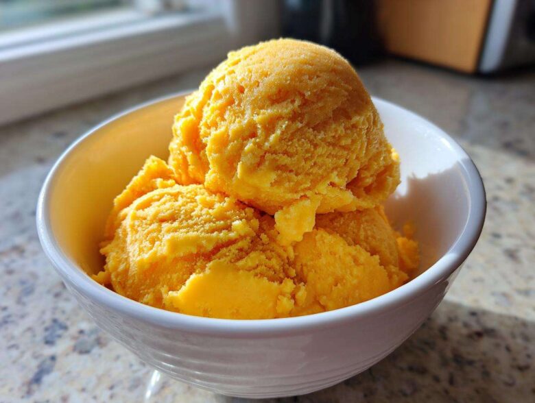 Three bright orange scoops of Vegan Mango Pineapple Sorbet served in a white dessert bowl.
