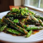 Close-up of Vegan Spring Vegetable Stir Fry with Ginger featuring glossy asparagus spears and scallions topped with sesame seeds.