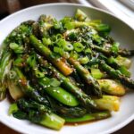 Close-up of Vegan Spring Vegetable Stir Fry with Ginger featuring asparagus, bok choy, and sesame seeds.