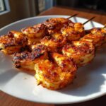Close-up of perfectly cooked Air Fryer Crispy Cajun Shrimp Skewers on a white plate, showing a vibrant orange-red spice coating.