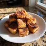 A pile of golden Air Fryer Crispy Cinnamon French Toast Bites coated in sugar on a white plate.