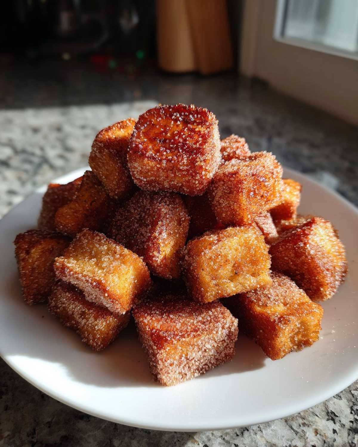 A close-up of golden brown Air Fryer Crispy Cinnamon French Toast Bites piled high on a white plate.