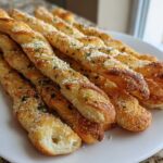 A stack of golden, twisted Air Fryer Crispy Garlic Breadsticks topped with grated Parmesan and parsley on a white plate.