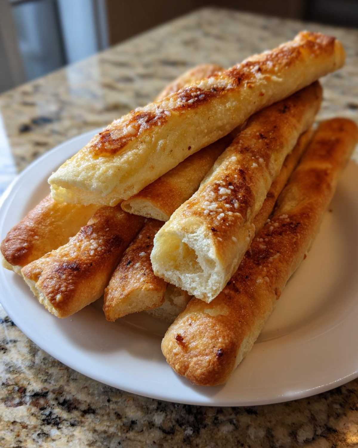 A stack of golden brown Air Fryer Crispy Garlic Breadsticks sprinkled with Parmesan cheese on a white plate.
