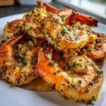 A close-up of juicy Air Fryer Crispy Garlic Butter Shrimp coated in melted butter, garlic, and parsley on a white plate.