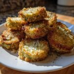 A stack of golden brown Air Fryer Crispy Garlic Dill Pickles slices dusted with herbs and salt on a white plate.