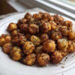 A pile of golden brown, crispy Air Fryer Crispy Garlic Herb Chickpeas seasoned with herbs on a white plate.