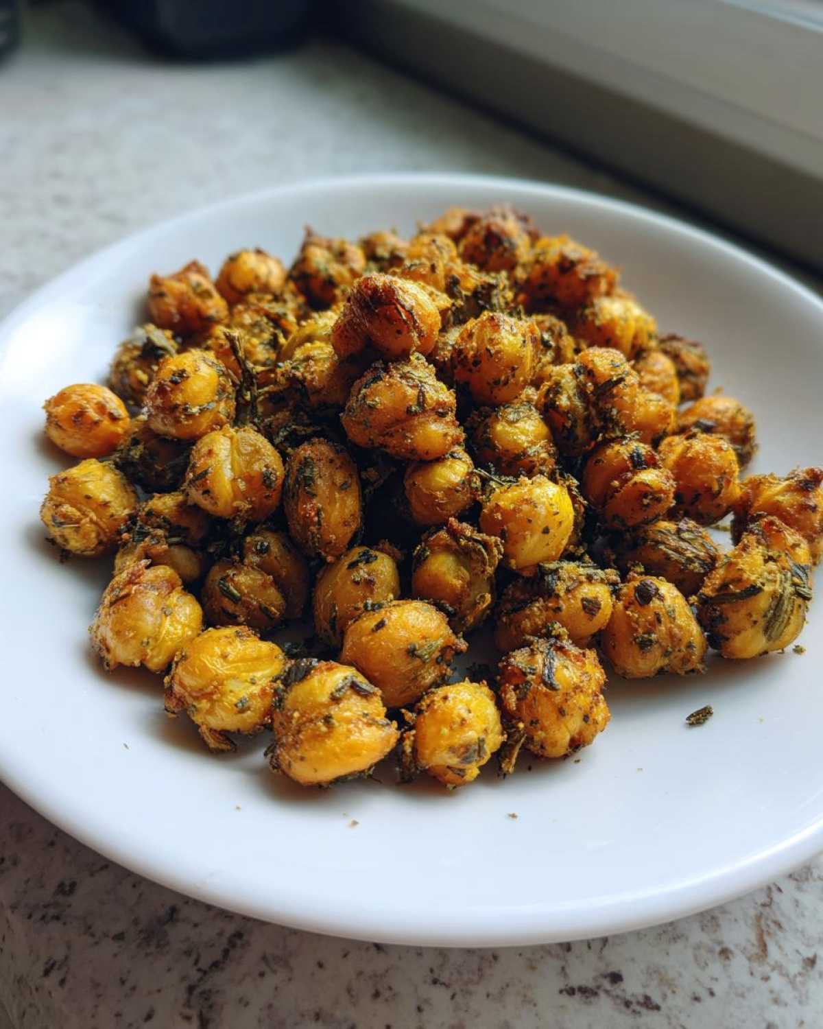 A close-up of golden brown, crispy Air Fryer Crispy Garlic Herb Chickpeas piled on a white plate.