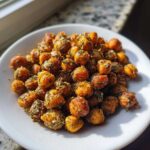 A white plate piled high with golden brown, crispy Air Fryer Crispy Garlic Herb Chickpeas seasoned with visible green herbs.