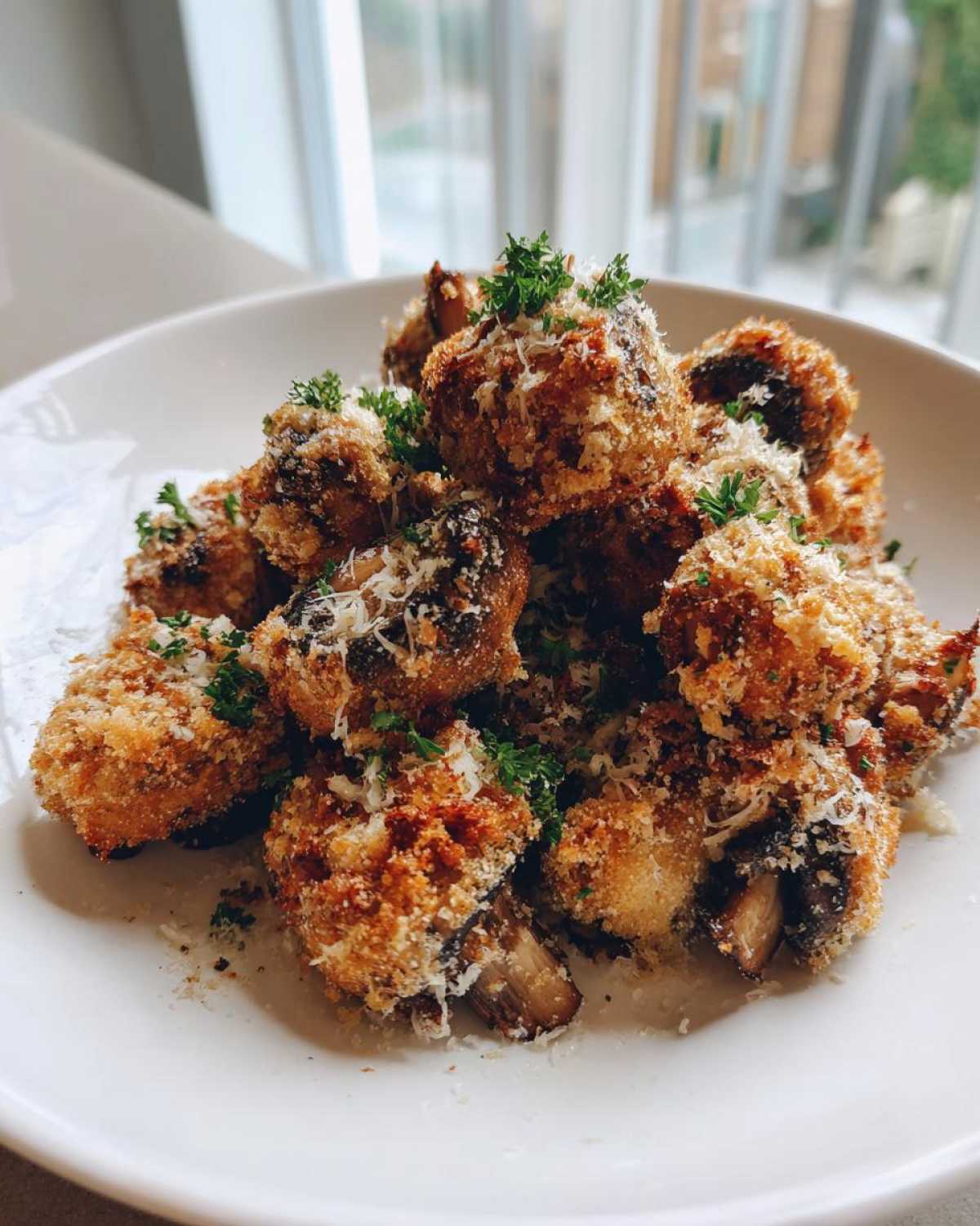 A white plate piled high with Air Fryer Crispy Garlic Parmesan Mushrooms, topped with grated cheese and parsley.