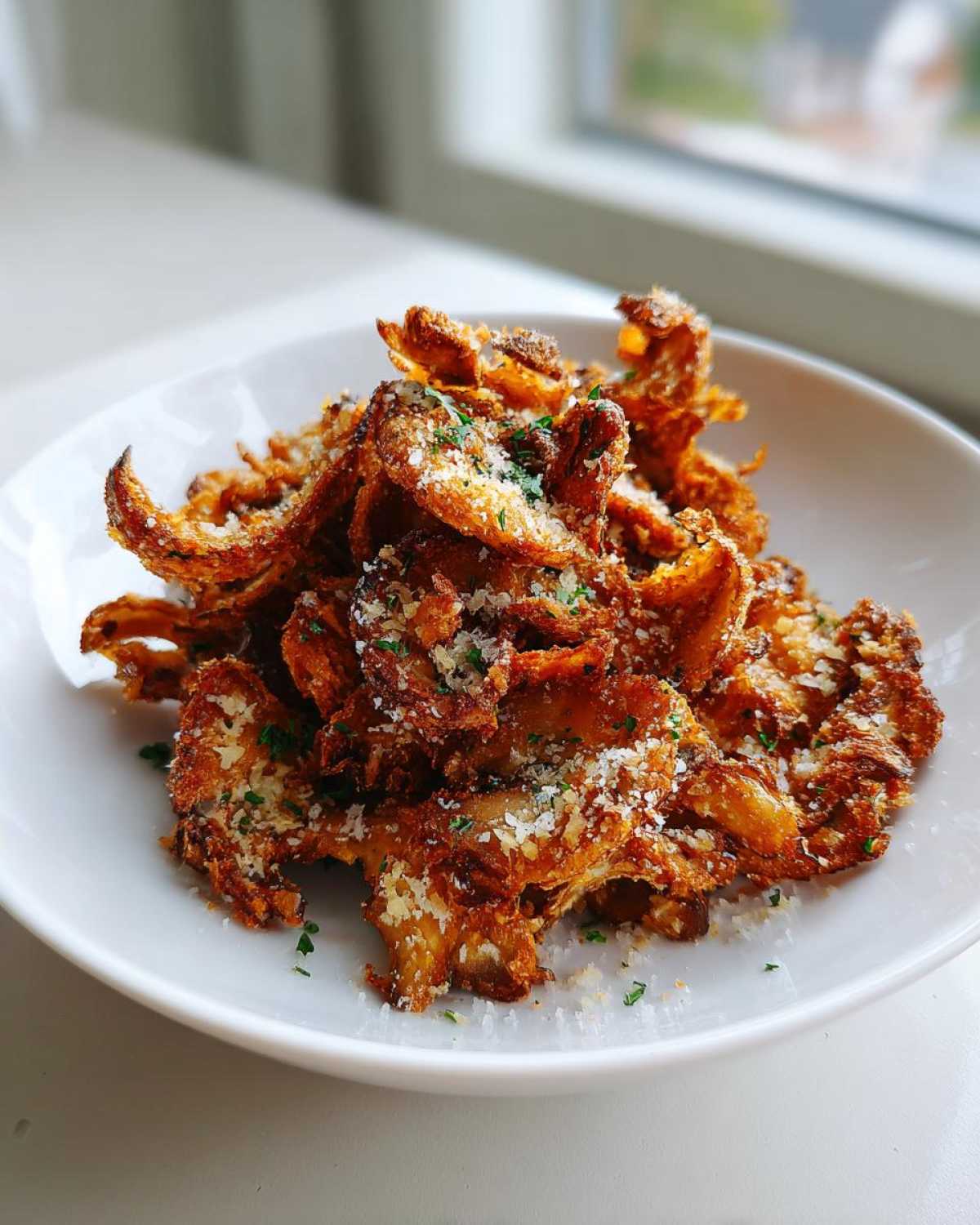 A white bowl filled with crispy, golden-brown Air Fryer Crispy Garlic Parmesan Mushrooms, topped with grated cheese and parsley.