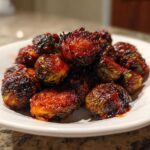 A white bowl filled with glossy, caramelized Air Fryer Crispy Gochujang Brussels Sprouts, showing charring and a rich red glaze.
