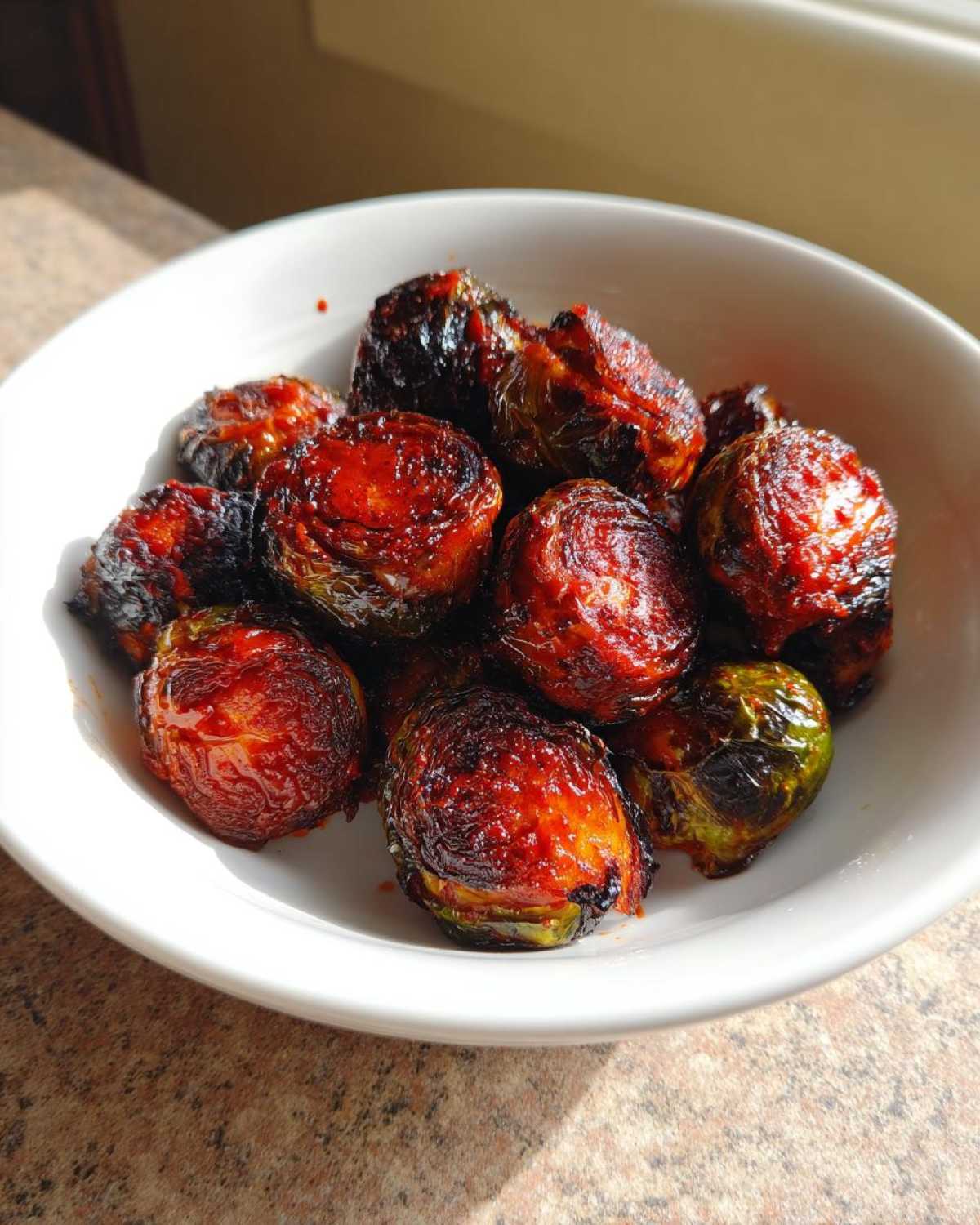 Close-up of crispy, caramelized Air Fryer Crispy Gochujang Brussels Sprouts served in a white bowl.