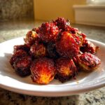 A close-up of a pile of Air Fryer Crispy Gochujang Brussels Sprouts, glazed dark red and caramelized.