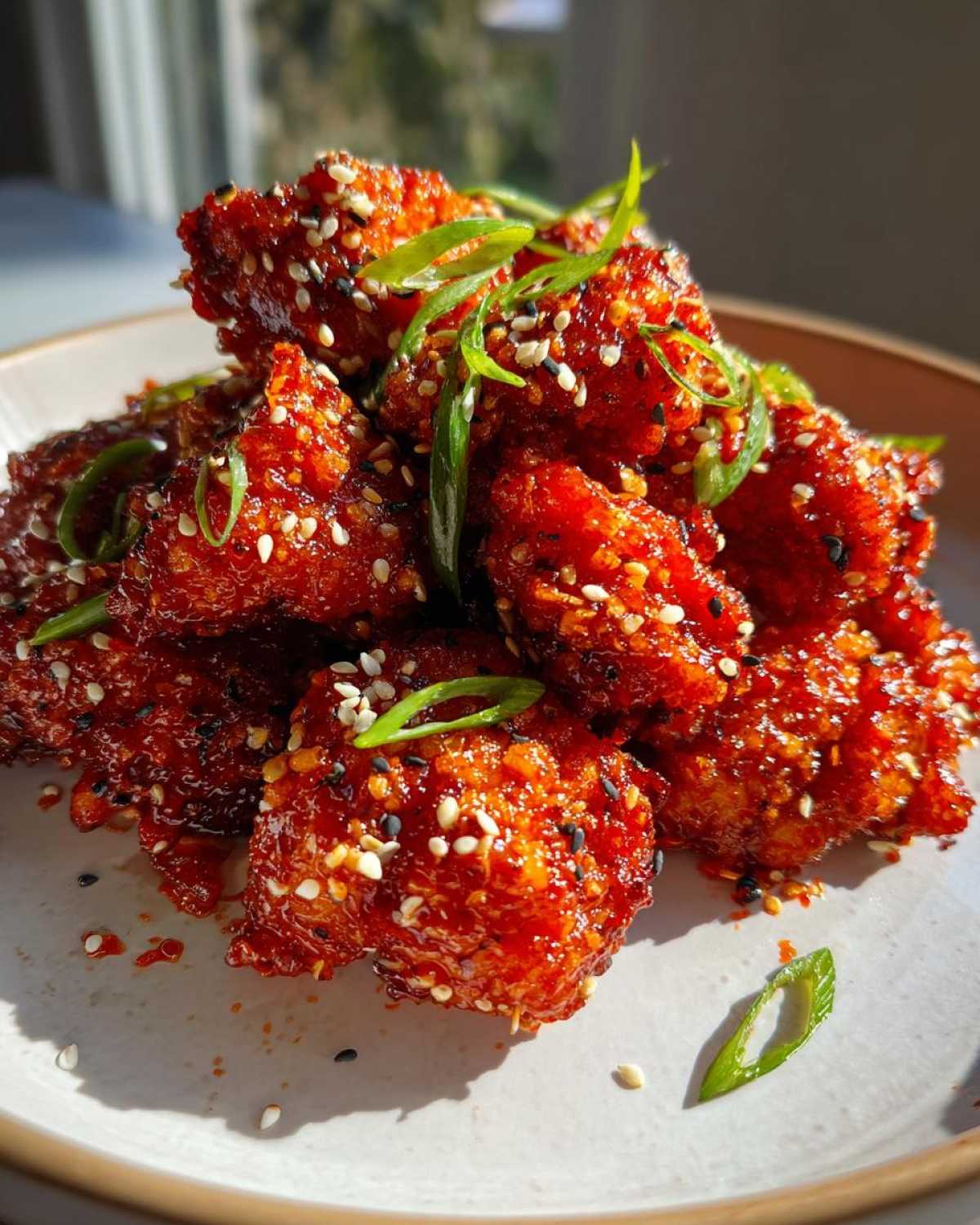 A pile of sticky, bright red Air Fryer Crispy Korean Chicken Bites topped with sesame seeds and green onions.
