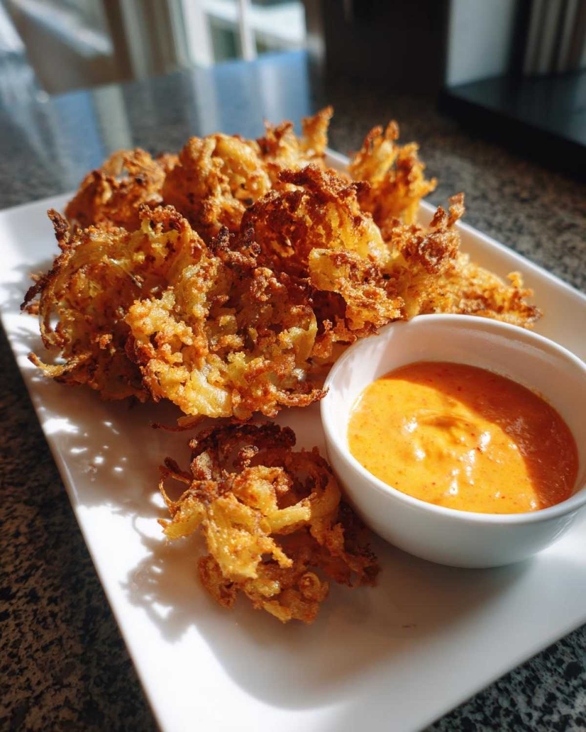 Golden brown Air Fryer Crispy Onion Petals served on a white plate next to a small bowl of vibrant orange spicy mayo.