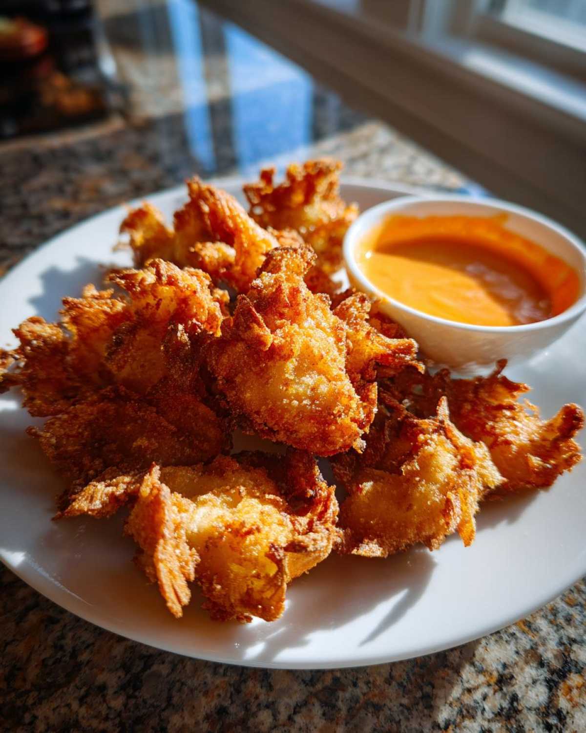 Golden brown, crispy Air Fryer Crispy Onion Petals served on a white plate next to a small bowl of spicy mayo dip.