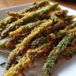 Close-up of golden brown Air Fryer Crispy Parmesan Asparagus Fries piled on a white plate.