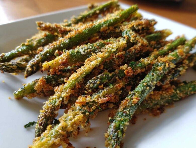 Close-up of golden brown Air Fryer Crispy Parmesan Asparagus Fries piled on a white plate.